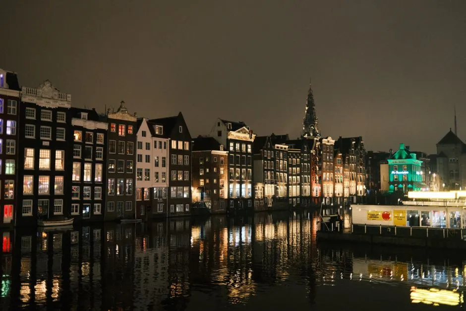 Row of Amsterdam canal houses with lit windows reflected in the water at night