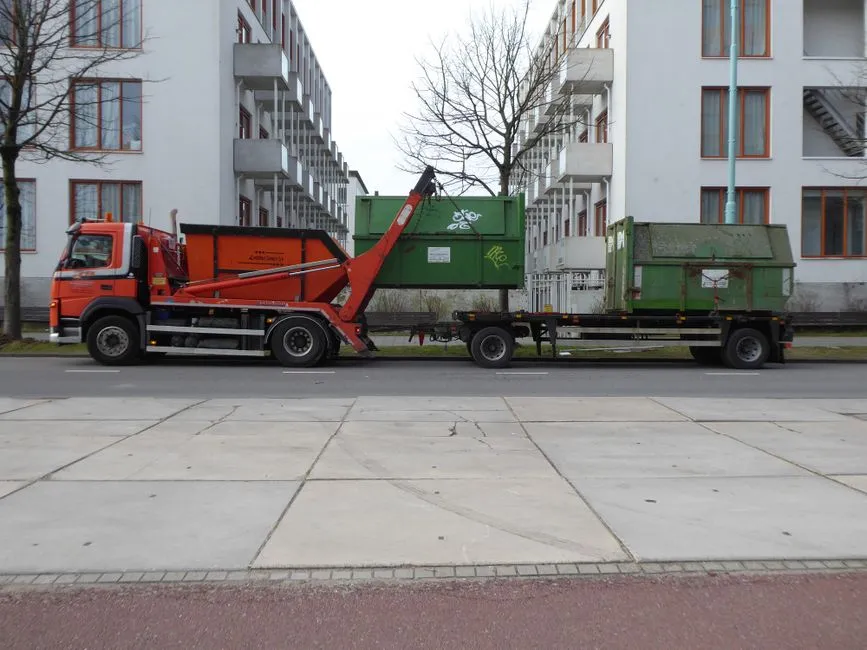 A specialized truck lifting a waste container out of the ground on a residential Amsterdam street