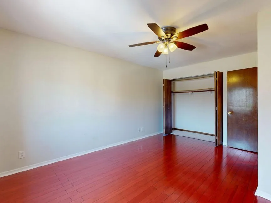 A spacious empty room with a wooden floor, a ceiling fan, and a closet with an open door, no people or readable text visible