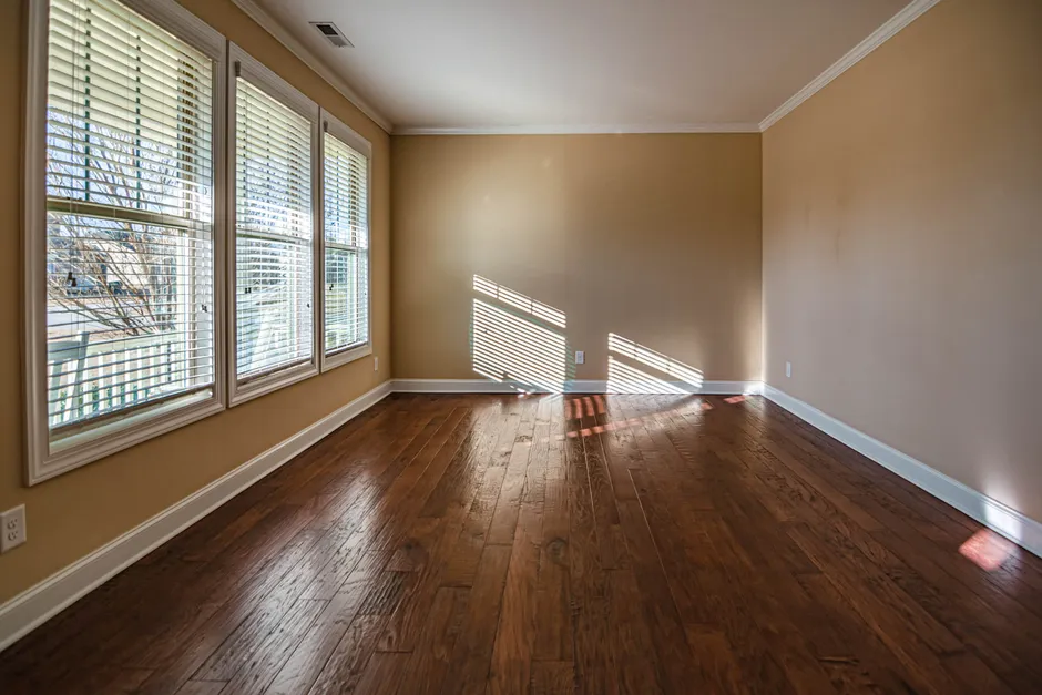 A bright, empty apartment room with large windows and hardwood flooring, no furniture or people visible