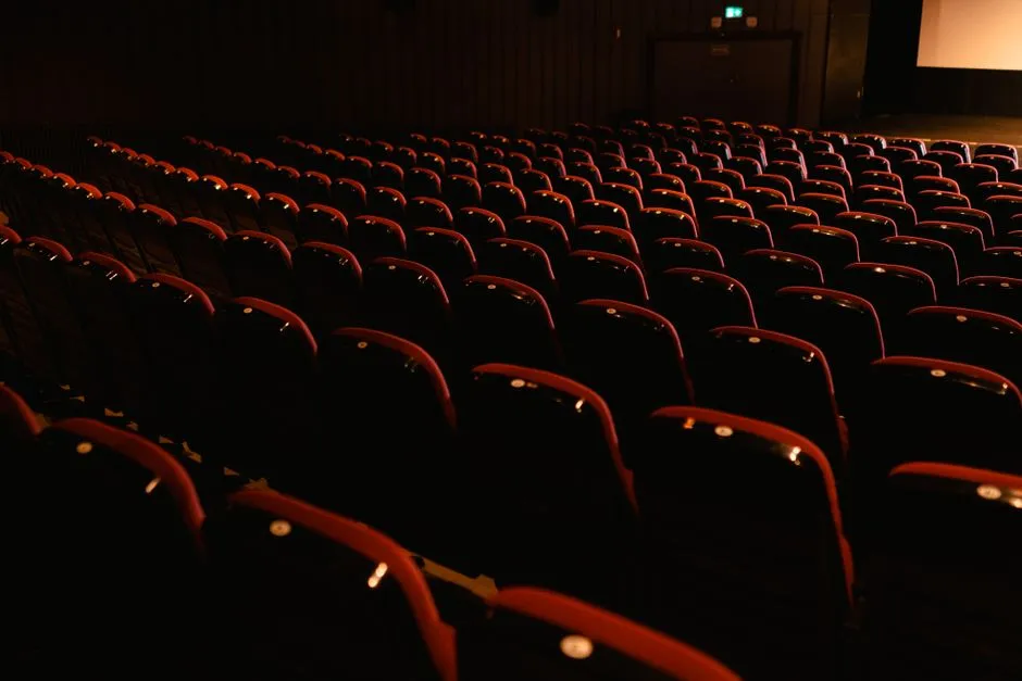 Rows of empty red cinema seats in a dark screening room, lit by a warm glow from the front of the theater