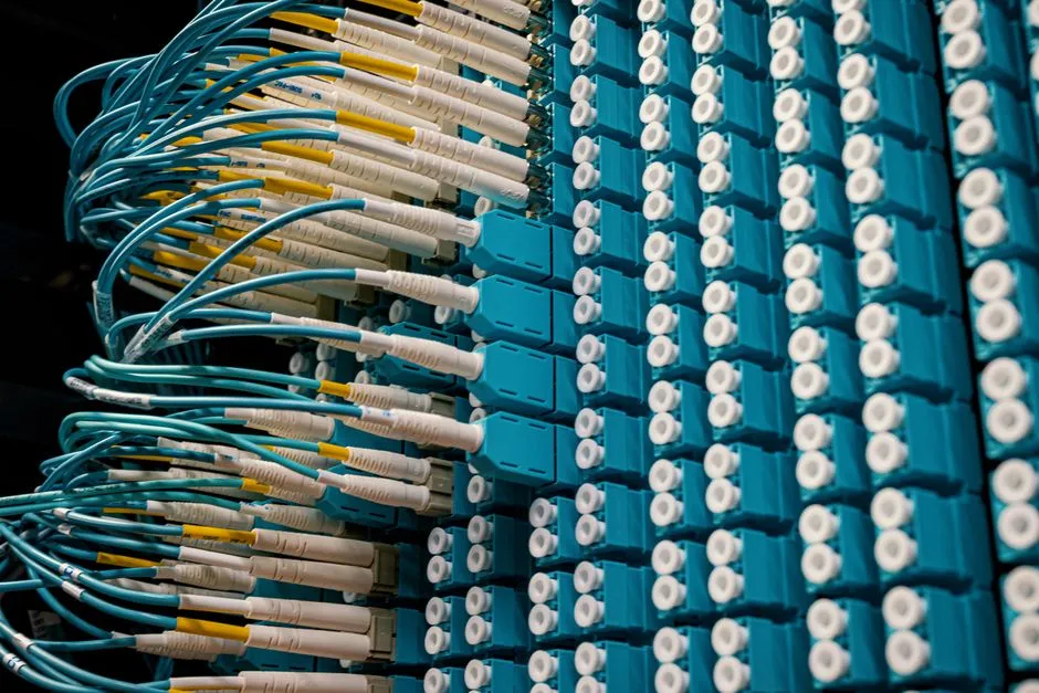 Rows of blue fiber optic patch panel connectors with cyan and white cables plugged into a telecommunications distribution frame