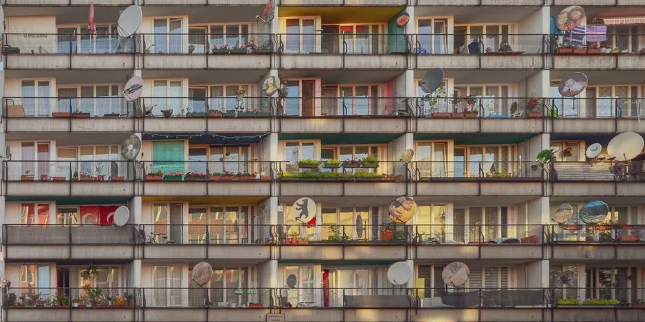 A GDR-era apartment block in Berlin with rows of balconies, satellite dishes, and potted plants on nearly every floor