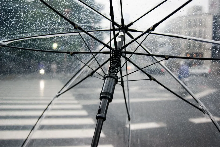 A clear umbrella held up against heavy rain over a city crosswalk, protecting against the elements