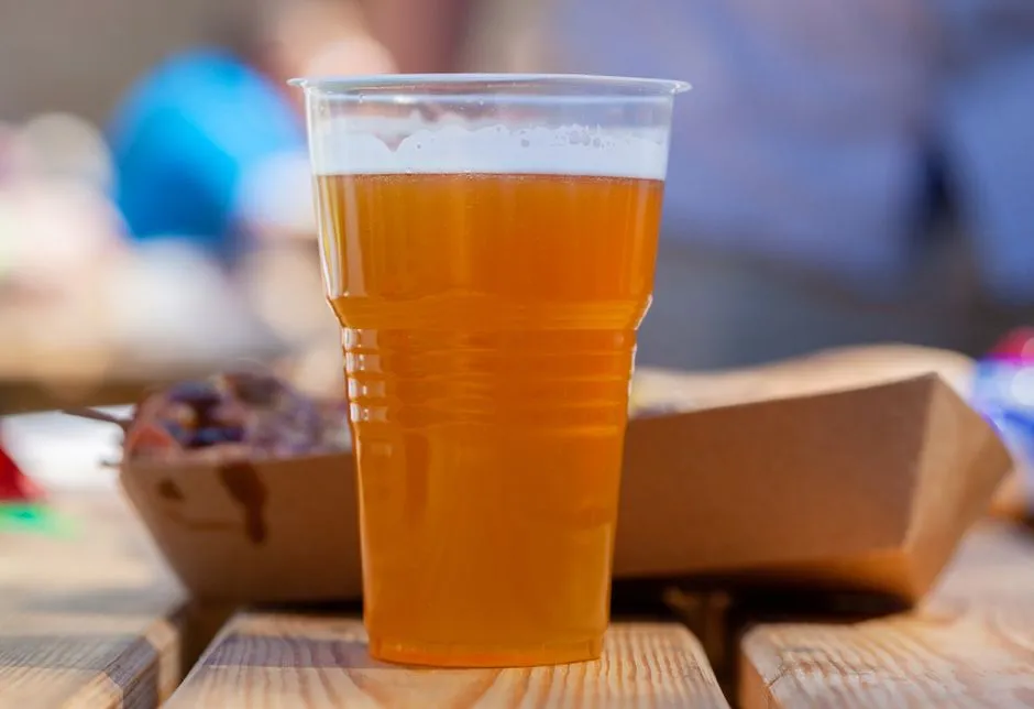 A plastic cup of beer with a takeaway food box on a wooden picnic table outdoors