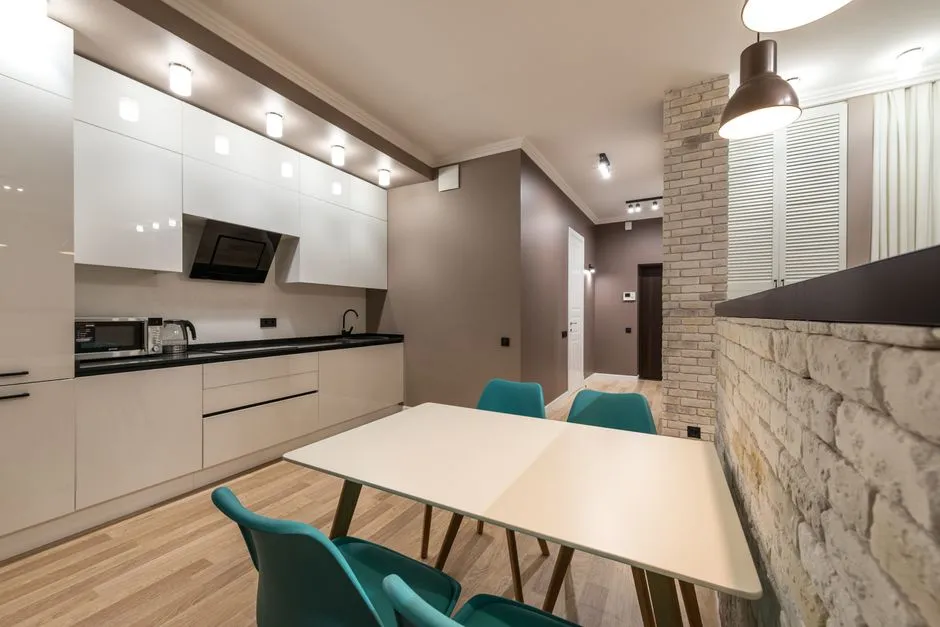 A modern fitted kitchen with white cabinets, a dining table, and pendant lighting in a bright apartment