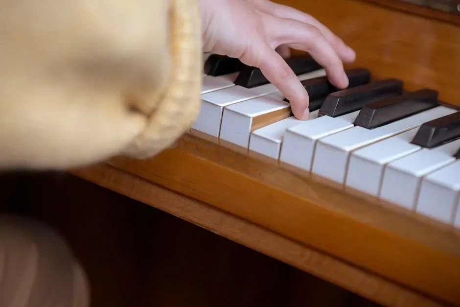 Close-up of a child's hand pressing piano keys on a wooden upright piano during a lesson, soft focus on a sleeve in the foreground, no face visible