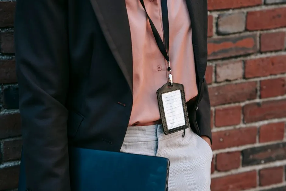 A dark leather ID badge holder and lanyard hanging against a blazer, with a folder tucked underneath