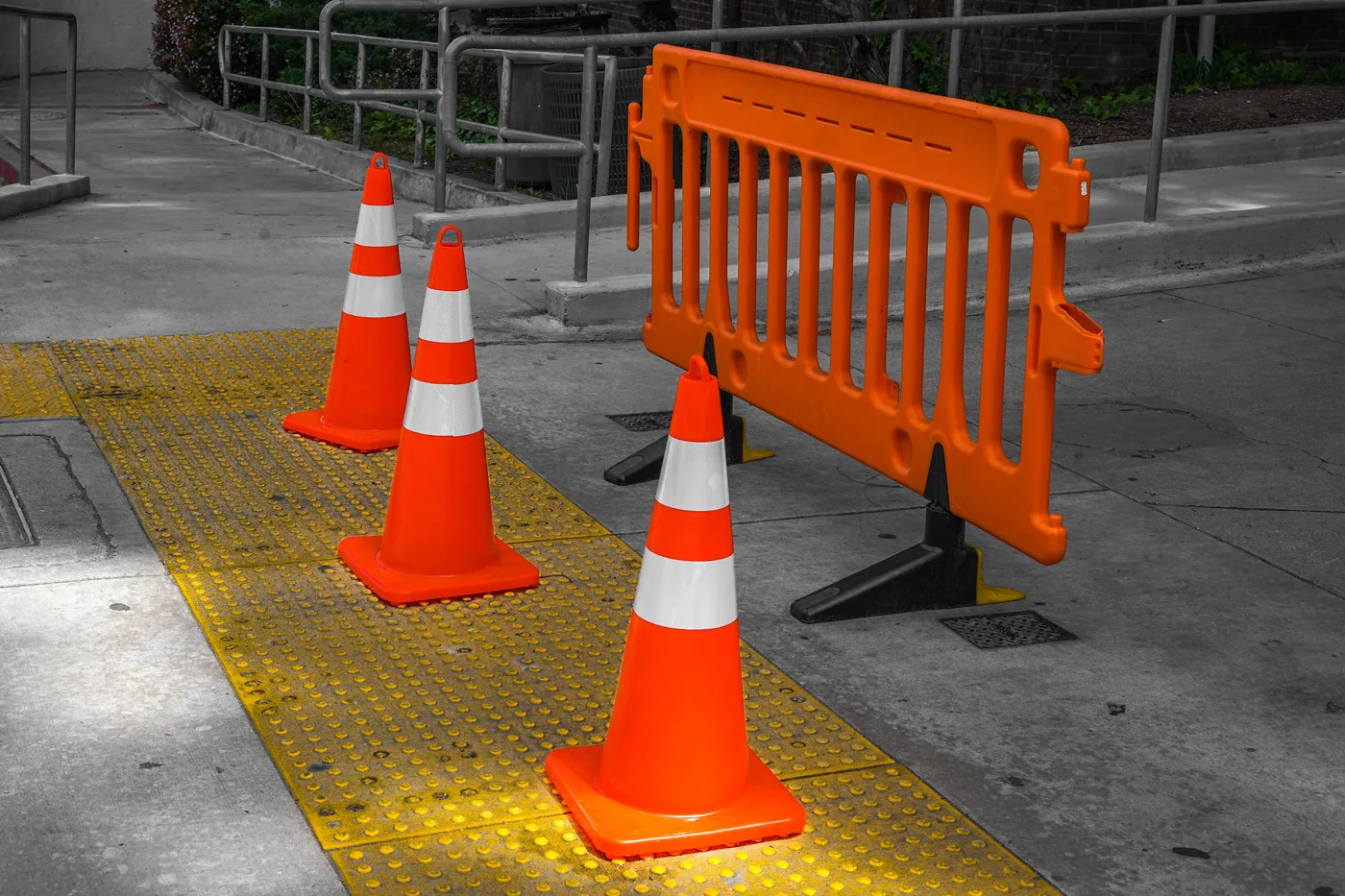 Orange traffic cones and a plastic barrier gate blocking a paved walkway, no vehicles, signage, or people visible