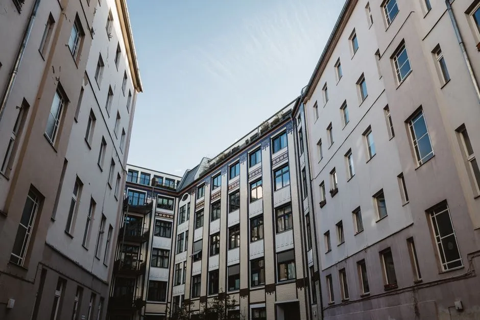 A Berlin residential courtyard seen from below, rows of apartment building facades and windows on both sides typical of the city's rental housing stock