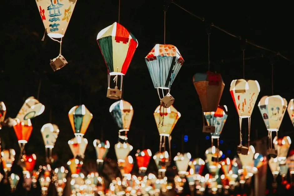 Colorful hand-painted paper lanterns shaped like small hot air balloons, strung on lines and glowing at night, decorated with simple childlike drawings