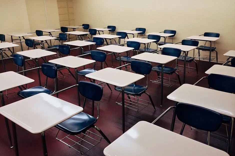 Rows of empty school desks with attached chairs arranged in a plain classroom, no people or readable text visible