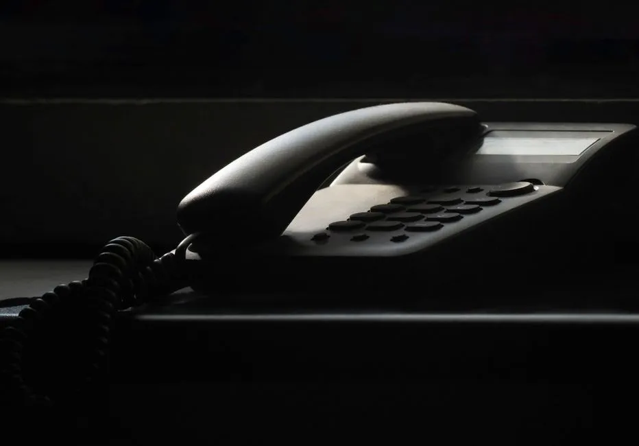 A dark, shadowed office telephone with its handset resting on the base, lit by a narrow shaft of light