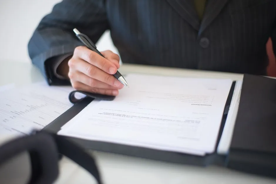 A person in a business suit signing a document on a clipboard with a pen