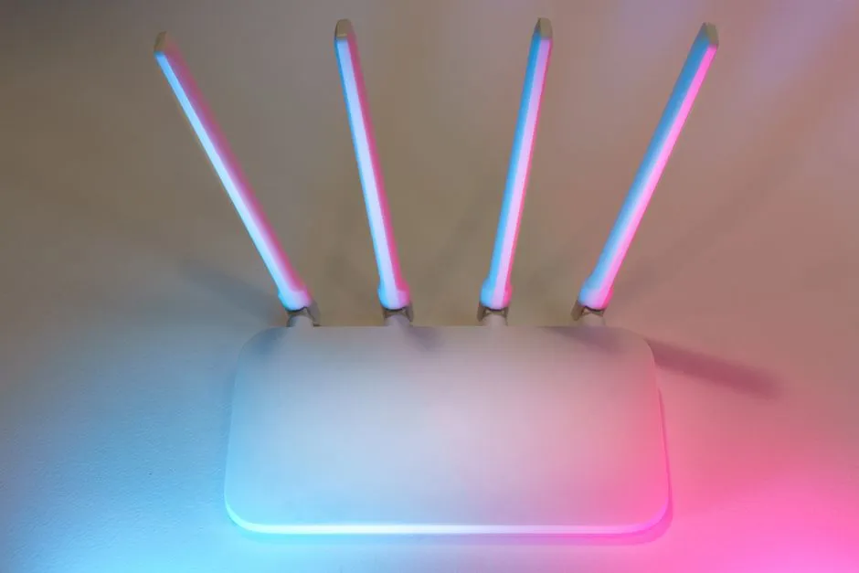 A white wireless router with four antennas raised, lit from below by pink and blue ambient light