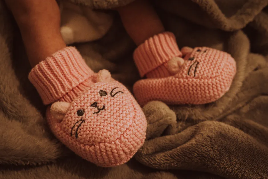 A newborn's bare feet wearing a pair of pink knitted booties, wrapped in a soft blanket