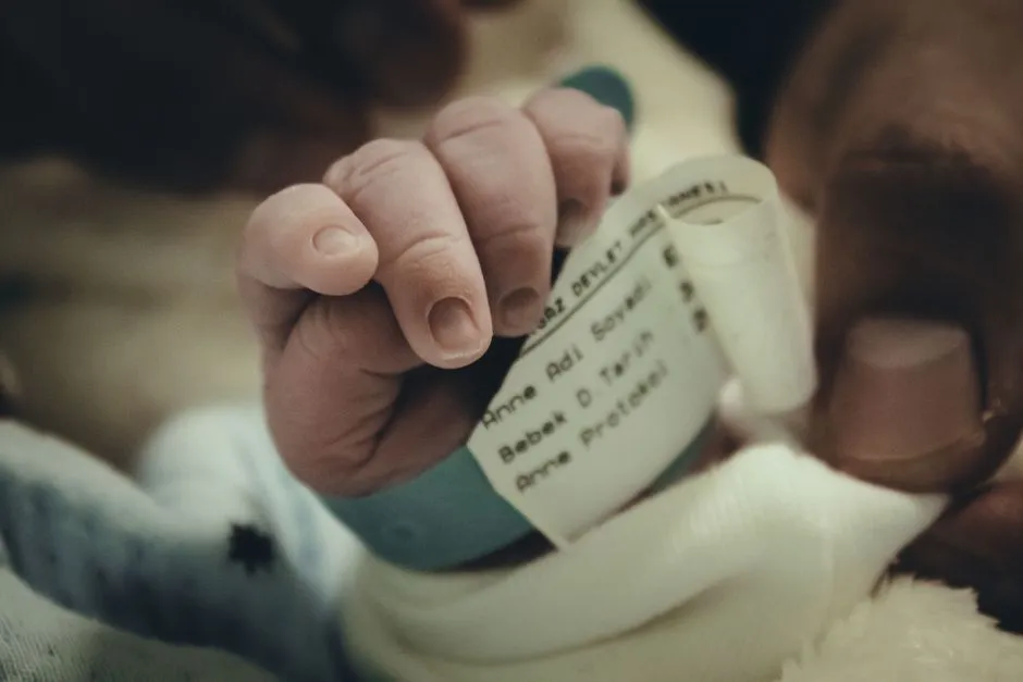 A newborn's hand gripping a hospital identification wristband, a knit baby sock visible alongside