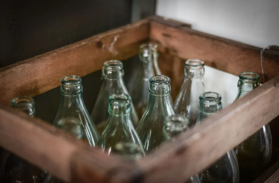A dozen empty glass bottles standing upright inside an old wooden crate, the type of returnable Mehrweg container used in Germany's Pfand system