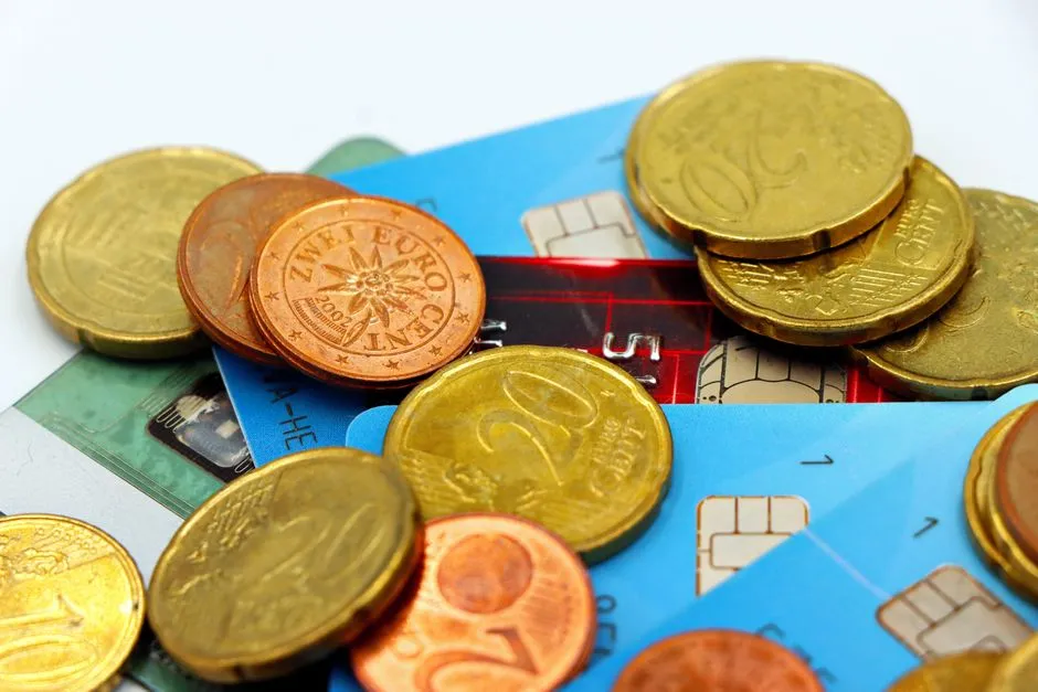 Monedas de euro esparcidas sobre dos tarjetas bancarias en un fondo claro