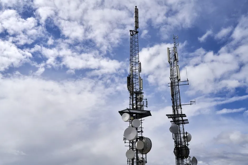 Two tall broadcast transmission towers with satellite dishes and antennas, seen against a blue sky with scattered clouds