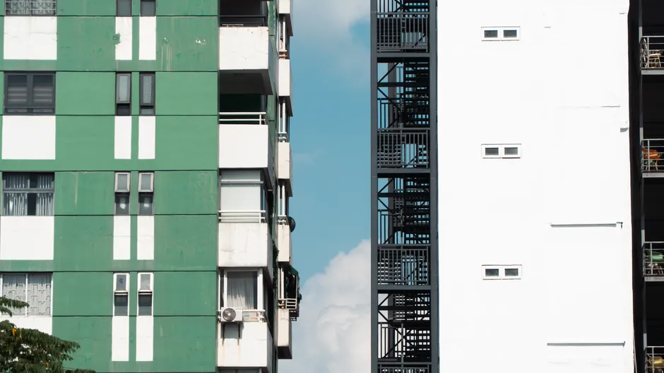 Balkonları, küçük pencereleri ve dış yangın merdiveni olan, kontrastlı yeşil ve beyaz bir apartman cephesi