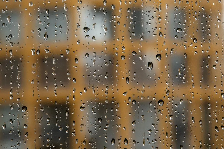 Rain drops covering a window pane with blurred building windows visible through the glass behind it