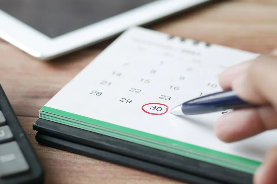 A hand circles a date on a desk calendar in red pen, marking a deadline