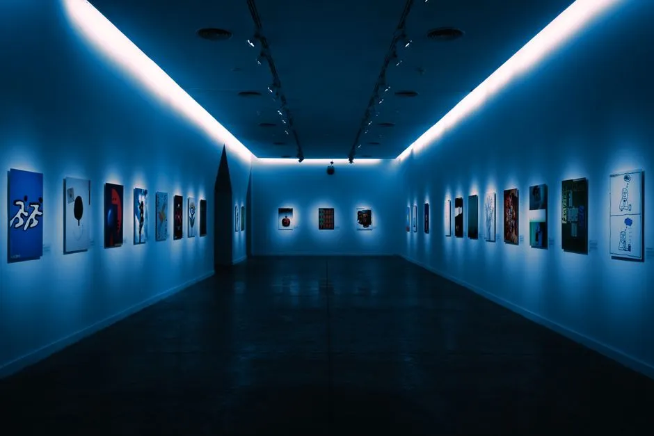 A dim museum gallery corridor lined with small framed artworks under soft blue overhead lighting, no people visible