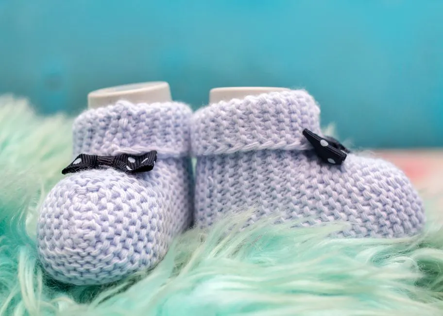 A pair of hand-knitted light blue baby booties resting on soft faux fur