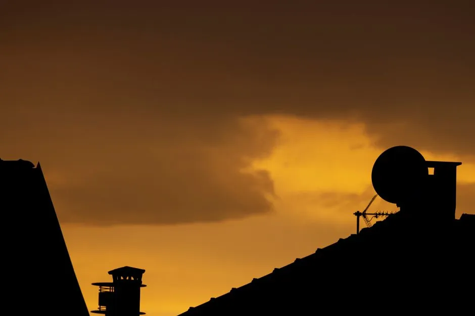Silhouettes of a rooftop TV antenna and satellite dish against a glowing orange sunset sky