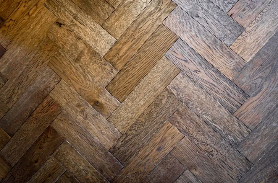 A close-up of a herringbone-pattern wood parquet floor in an older apartment