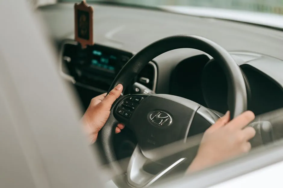 A person's hands resting on a car steering wheel while driving