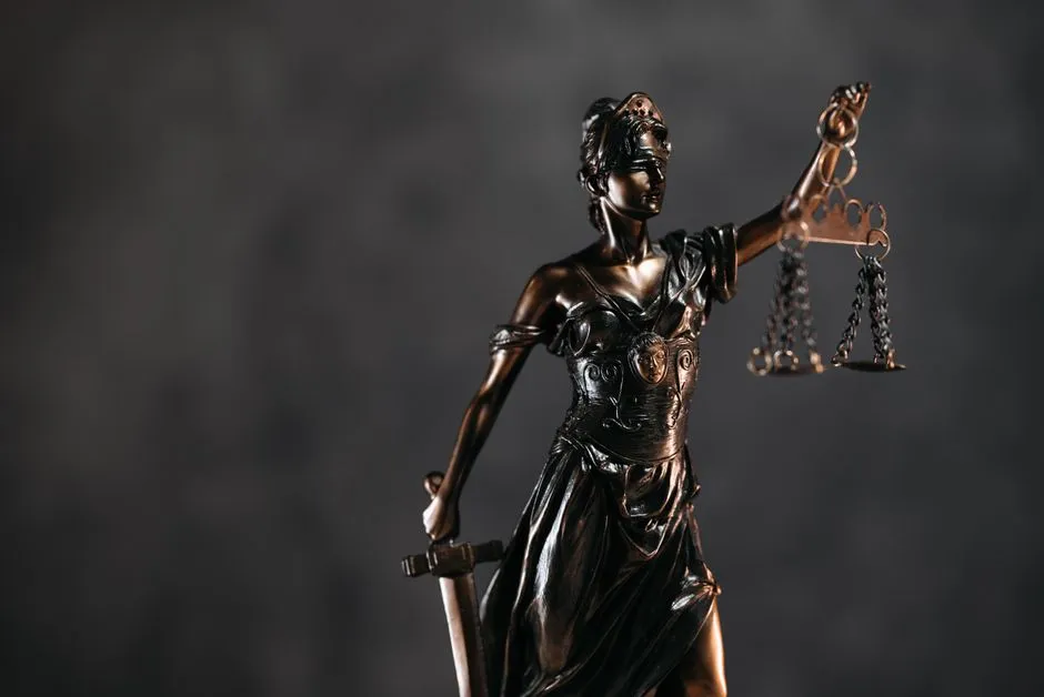 A bronze Themis statue, blindfolded and holding a set of scales and a sword, against a dark background