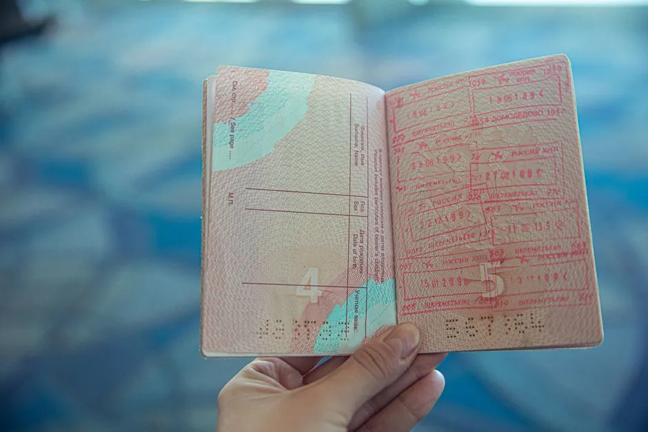 A hand holds open a passport showing pages full of entry and visa stamps