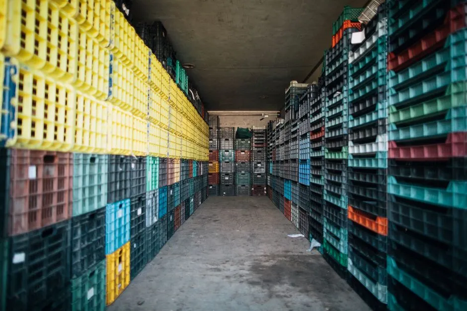 Filas de cajas de bebidas de plástico apiladas en distintos colores a lo largo de un pasillo de almacén