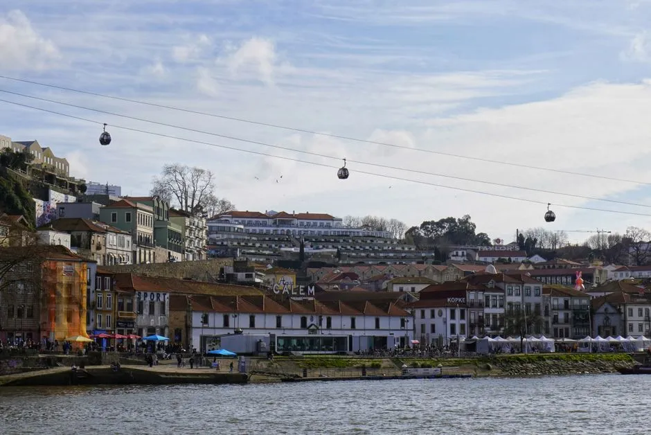 A cable car gondola suspended over a river with a city skyline in the background