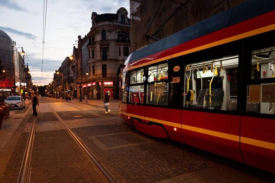 A modern light rail tram passing along a city street lined with buildings