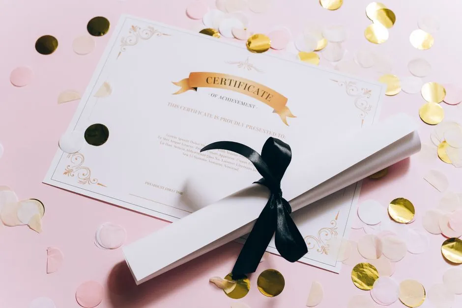 A rolled certificate tied with a ribbon next to a printed certificate, surrounded by confetti