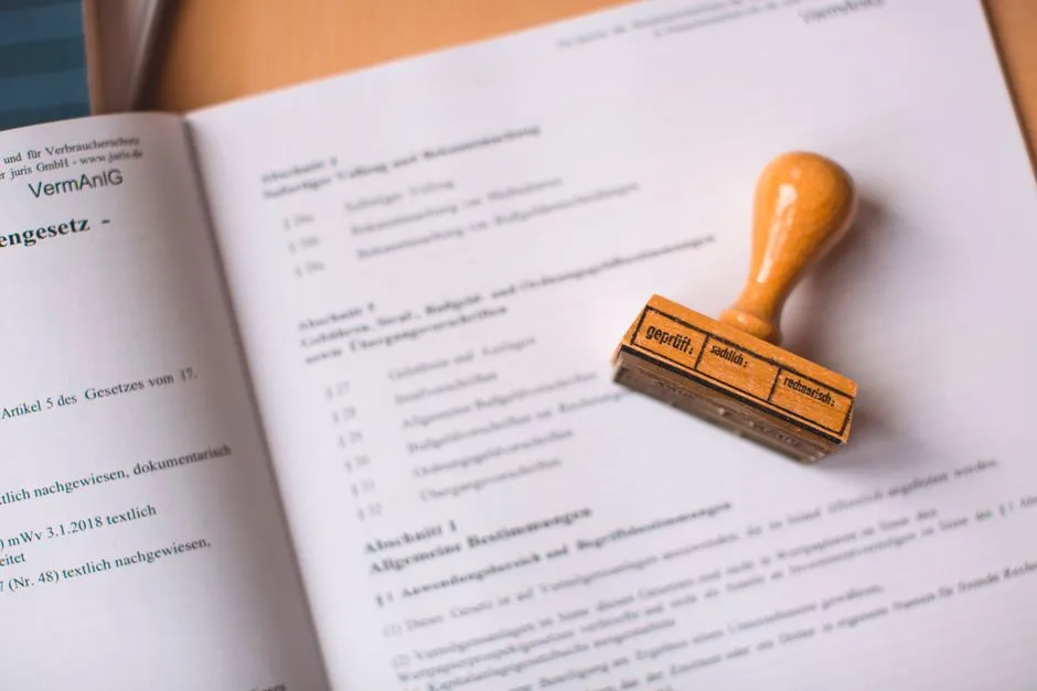 A German legal statute book lying open with a wooden 'geprüft' rubber stamp resting on the page