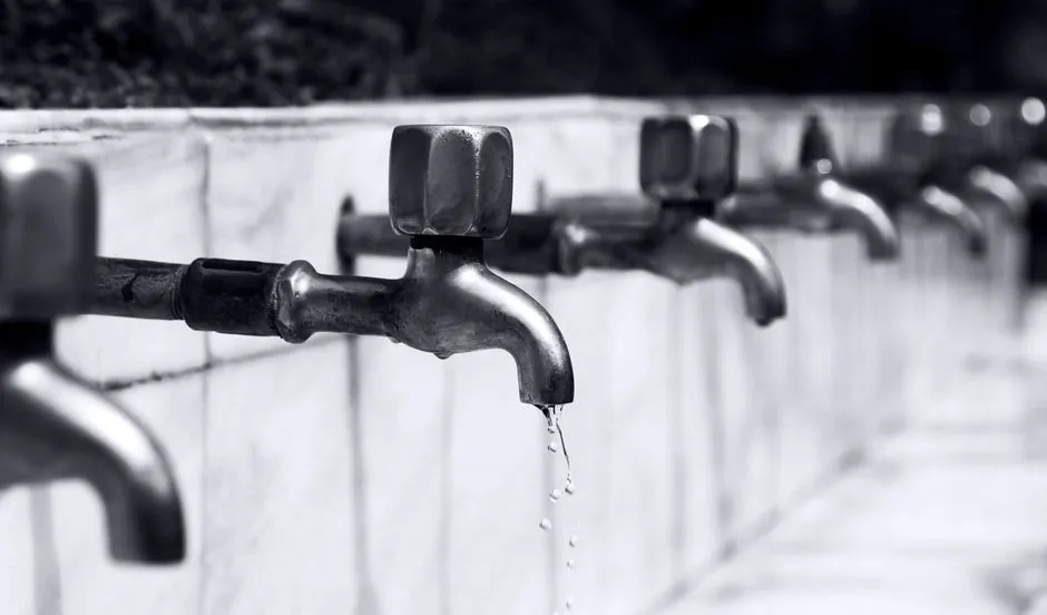 A row of metal water taps with water dripping from one of them