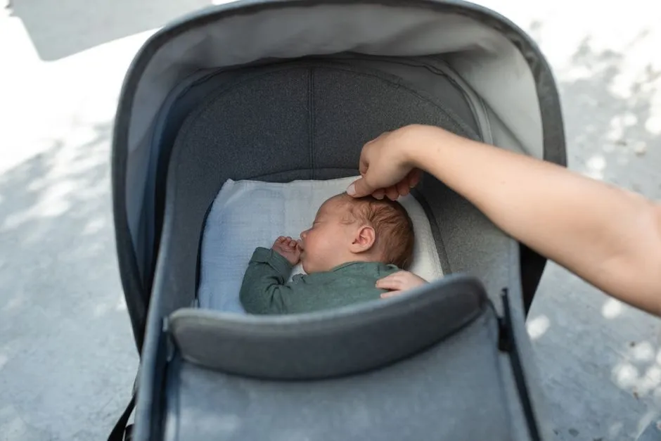 A parent's hand resting on a sleeping baby's head inside a stroller