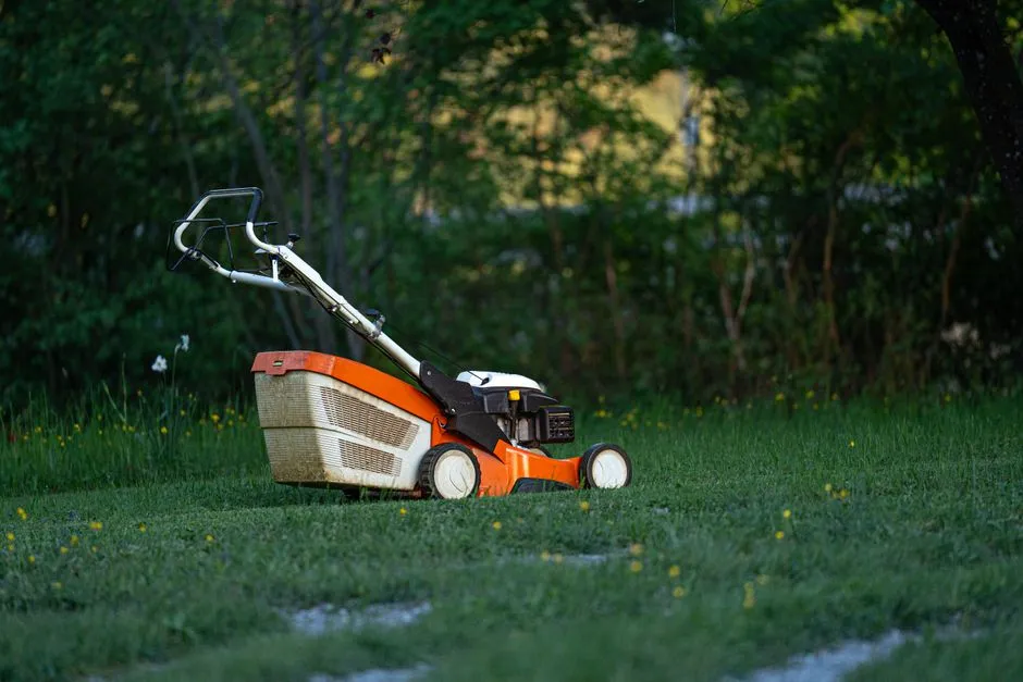An orange push lawn mower standing idle on a trimmed lawn in the evening light