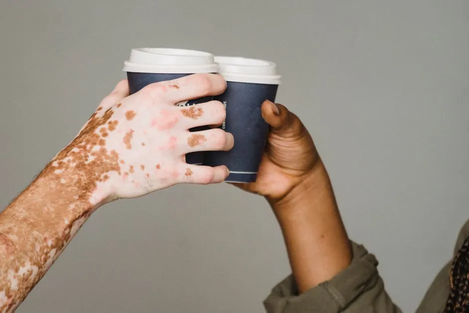 Two hands, one lighter-skinned and one darker-skinned, clinking two paper coffee cups together against a plain gray background