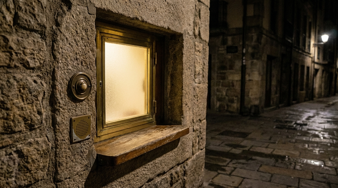 A softly lit pharmacy night service window built into a wall at night, with a small illuminated sign and a service bell, seen from outside, no people visible