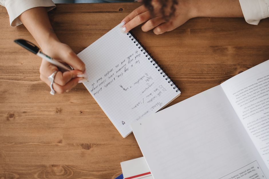 Close-up of a hand writing German vocabulary notes in a spiral notebook