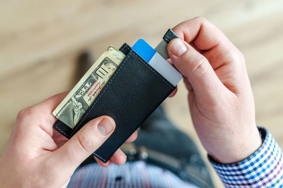 A hand pulling a bank card out of a slim wallet that also holds a folded banknote