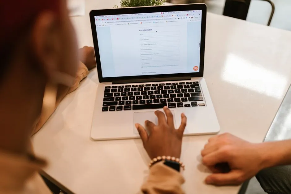 Two people looking at an online personal information registration form on a laptop