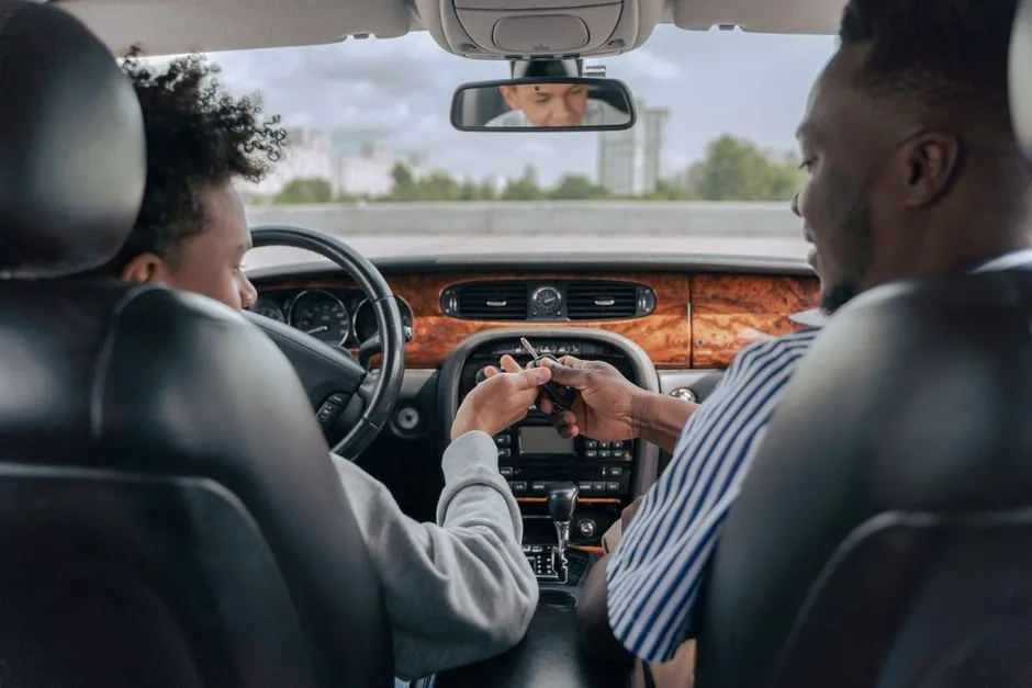 A passenger hands over car keys to the driver in the front seat of a car