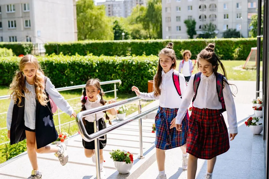 Children with backpacks walking into a primary school building on a sunny morning